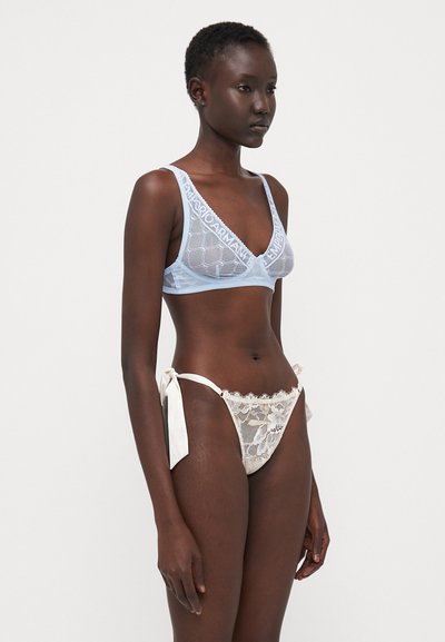 Bralette in pizzo blu chiaro con dettaglio del logo e perizoma bianco in pizzo con fiocchi, che mettono in mostra intricate trame e texture.
