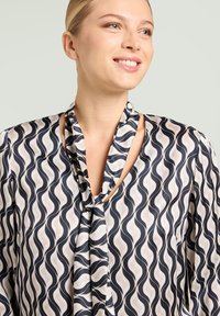 Flydende bluse med et sort og hvidt bølget mønster, lavet af et glat stof med bindedetalje ved halsen og et afslappet design.