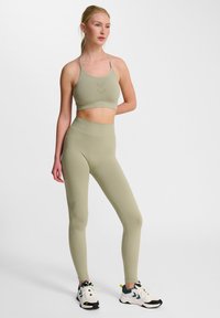 Olivgrön sport-bh och högmidjade leggings i matt tyg, med ett zigzagmönster på bh:n och på leggingsens sida. Bärs med vita sneakers.