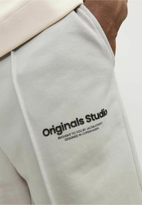 Pantalones de chándal gris claro, fabricados en un tejido suave, con un estampado de logo negro en el lateral, cintura cómoda y diseño ajustado.