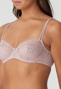 Koronkowy biustonosz balconette w delikatnym różu z przezroczystego materiału, ozdobiony szczegółowym haftem i falistymi krawędziami. Cienkie regulowane ramiączka oraz wsparcie w postaci drutów.
