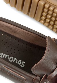 Braune Lederbootsschuhe mit einer flexiblen Gummisohle, perforierter Einlegesohle und kontrastierenden Nähten. Mit einem auffälligen Logo innen.