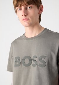 Pelēka kokvilnas T-kreklā ir spilgti izcelts, reljefs "BOSS" logo tumšākā nokrāsā. Ar īsām piedurknēm un apaļu kakla dizainu, tam ir mīksta tekstūra.