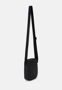 Bolso cruzado negro hecho de material suave, con forma rectangular, correa ajustable y cierre con cremallera. Diseño y textura sencillos.