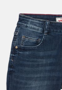 Jeans in denim blu scuro, con una texture sbiadita, tasca frontale con dettagli di cucitura e un'etichetta del marchio visibile in vita.