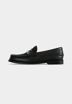 Mocassin pour homme en cuir noir avec une tige tissée et un petit talon, vu de côté sur un fond blanc uni.