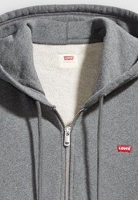 Felpa grigia con zip Levi's, dotata di coulisse, zip in metallo e piccolo logo rosso Levi's sul lato sinistro del petto.