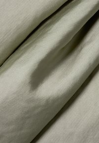 Tessuto color verde oliva chiaro con una texture liscia, caratterizzato da pieghe diagonali e un sottile lucentezza, che mette in mostra la sua struttura intrecciata.