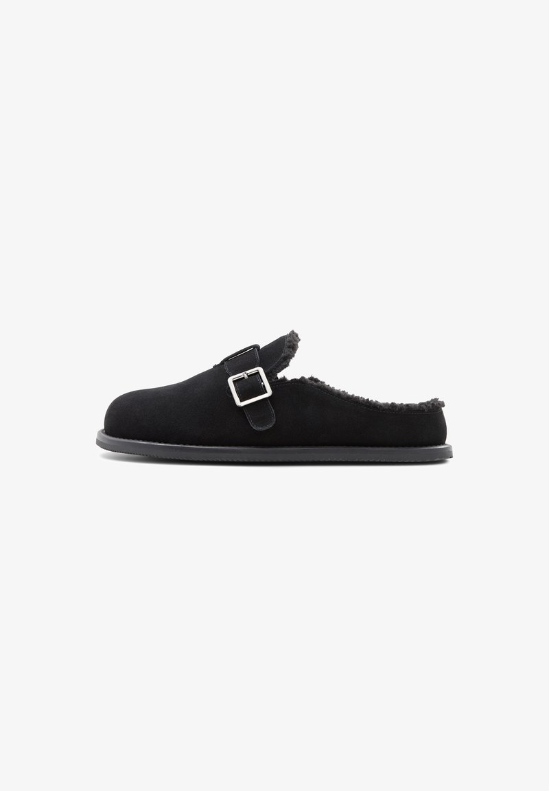 Black suede slip-on slippers with a buckled strap, shearling lining, and a rubber sole; rounded toe and backless design.