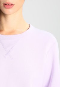 Ljust lavendelfärgad sweatshirt med rundad halsringning, ribbat mönster och korsstygn på axelsömmen.