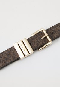 Brauner Lederuhrensand mit strukturierten Oberflächen, goldfarbener Metallschnalle und Michael Kors-Logo auf dem Verschluss.
