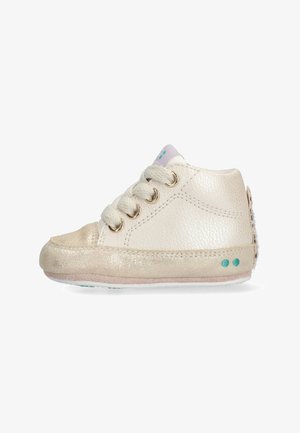 Cream leather sneaker with gold accents, round toe, three lace eyelets, and a soft sole. Features a textured back and teal dots on the side.