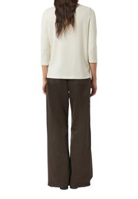 Jasnokremowa bluzka z długim rękawem i okrągłym dekoltem, zestawiona z luźnymi ciemnobrązowymi spodniami z tylnymi kieszeniami i gładką fakturą.