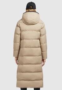 Beige pufferjakke med en lang silhuet, hætte og quiltet tekstur. Har en sort detalje på kraven og lange ærmer.