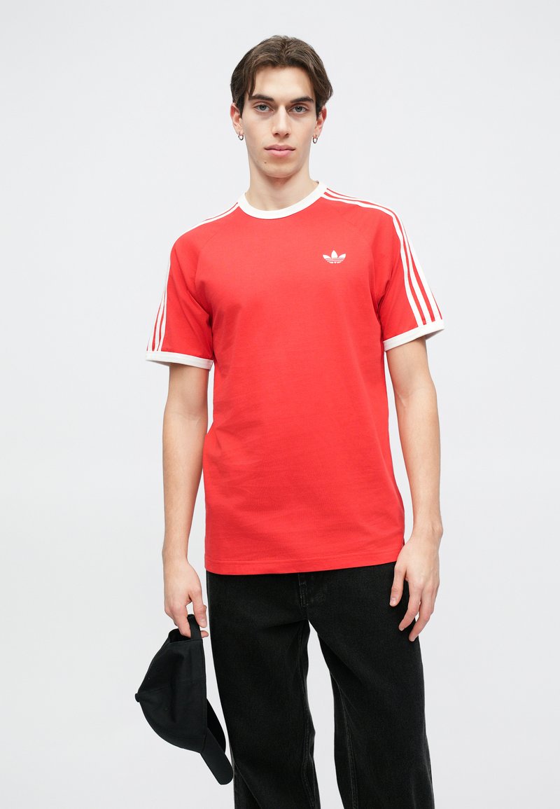 T-shirt rosso a maniche corte con accenti bianchi e tre strisce bianche su ogni spalla. Presenta un piccolo logo bianco sul petto.