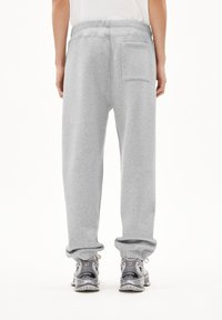 Grijze sweatpants met een relaxte pasvorm, elastische tailleband, ribgebreide boorden en een enkele achterzak. Gedragen met grijze sportschoenen.