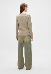 Beige knit sweater with textured sleeves, paired with wide-leg faded blue jeans. Sweater has ribbed cuffs and hem. Clean, minimalistic design.