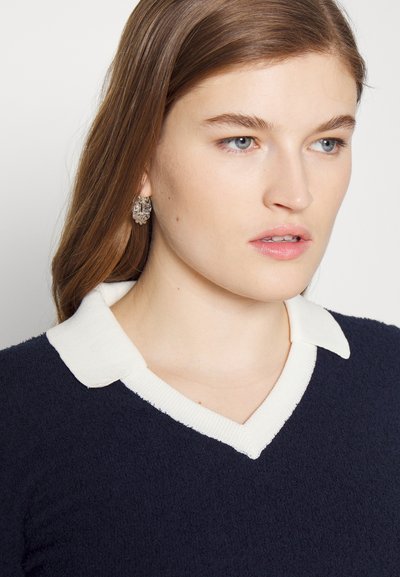 Suéter azul-marinho com colarinho branco canelado e design em V, apresentando um tecido texturizado. Brincos de argola decorativos e claros est�ão usados.