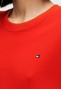 Κόκκινο φούτερ με στρογγυλό λαιμό και κοντά μανίκια. Διαθέτει μικρό κεντημένο λογότυπο σε μπλε, λευκό και κόκκινο στο αριστερό στήθος.