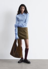 Hellblaues, geripptes Langarmshirt mit Kragen, olivegrüner Rock, braune, flauschige Handtasche, bordeauxrote Kniestrümpfe und schwarze Plateauschuhe.