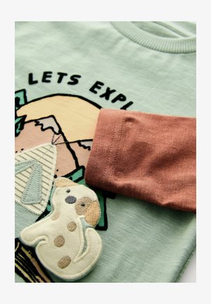 Tricou verde deschis cu un appliqué brodat în formă de câine, cu un accent de mânecă rozaliu și textul "HAIDE SĂ EXPLORĂM" deasupra unui design cu munte.