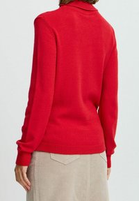 Maglione rosso lavorato a maglia con colletto e polsini a coste. Texture liscia con un design aderente, abbinato a una gonna in corduroy beige chiaro.