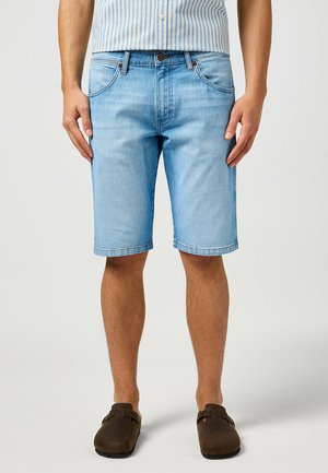 Light blue denim shorts with a straight cut, five pockets, and rolled hems. Paired with brown slip-on shoes and a striped shirt.