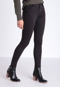 Jeans ajustados negros hechos de material elástico; con una cintura baja, cinco bolsillos y detalles de costura sutiles. Combinados con botas negras hasta el tobillo.