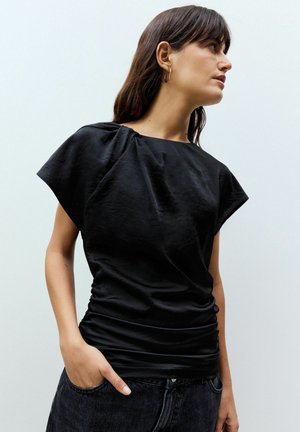 Black short-sleeve top with a gathered design on the shoulder, soft texture, and a slim fit, paired with high-waisted dark jeans.