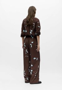 Combinaison marron avec motif floral bleu clair, présentant une coupe décontractée, des manches longues et une taille élastique. Tissu lisse avec une texture douce.