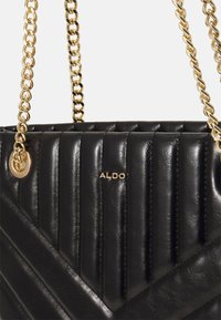 Sac à main noir matelassé avec des motifs verticaux et diagonaux, bandoulière chaîne dorée et logo embossé. Fabriqué en cuir texturé.