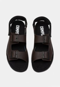 Brown sandals with adjustable buckles, open-toe design, and padded heel. Black insoles with logo detail. Textured material.