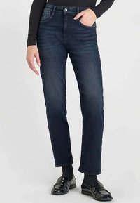 Jean en denim bleu foncé avec une coupe slim, jambes droites, conception à cinq poches et une ceinture dotée d'une fermeture classique par bouton et fermeture éclair.