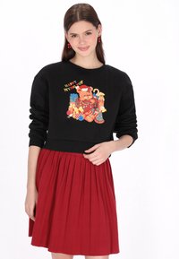 Fekete pulóver színes medve grafikával és ajándékokkal, piros pliszírozott szoknyával párosítva. Puha anyag, bordázott mandzsettákkal és szegéllyel.