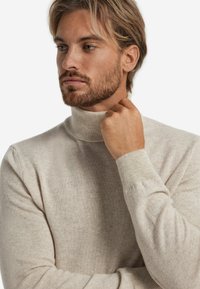 Jasno beżowy sweter z golfem, wykonany z miękkiej dzianiny. Posiada dopasowany krój oraz prążkowane mankiety, podkreślające czysty, minimalistyczny wygląd.