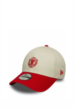 Beżowo-czerwona czapka bejsbolowa z logo Manchester United z przodu oraz emblematem New Era z boku, pokazana pod kątem na białym tle.