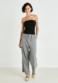 Top nero senza spalline, pantaloni a gamba larga grigi con righe sottili e pieghe frontali, indossati con zeppe in espadrilles color tan, su uno sfondo semplice.