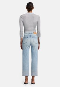 Maglione grigio a coste con lunghezza cropped e aperture laterali, abbinato a jeans azzurri chiari con orli decorati e design a gamba dritta.