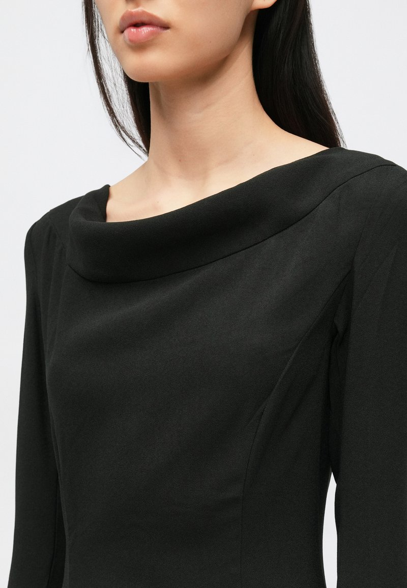 Vestito nero con scollo a cappuccio e maniche lunghe, realizzato in tessuto liscio e strutturato. Taglio aderente al corpo con dettagli minimi.