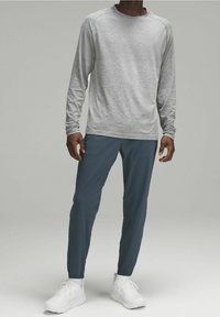 Szara koszula z długim rękawem o subtelnej fakturze, zestawiona z zwężającymi się ciemnoniebieskimi spodniami i białymi butami sportowymi.