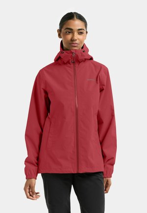Veste imperméable rouge avec fermeture éclair, capuche ajustable, poignets élastiques et logo sur la poitrine. Tissu lisse, design léger.