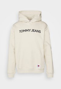 Sudadera de algodón color beige con un bolsillo frontal y un gran logotipo de "TOMMY JEANS". Presenta una capucha con cordón y puños de canalé.