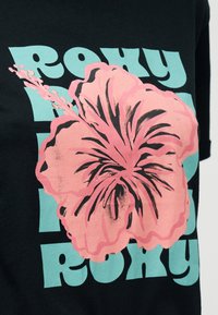 Μαύρο ύφασμα με μεγάλο ροζ λουλούδι ιβίσκου και έντονο φωτεινό μπλε στυλιζαρισμένο κείμενο που γράφει «ROXY» στο φόντο.