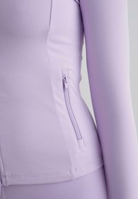 Světle fialový top s dlouhým rukávem vyrobený z hladkého, elastického materiálu, s boční kapsou na zip a čistými švy.