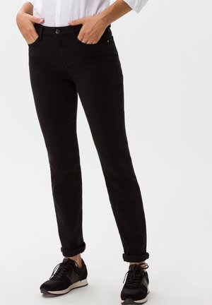 Pantalon en denim noir à coupe ajustée, avec une fermeture à bouton, un design à cinq poches et des ourlets retroussés pour un look décontracté. Associé à des baskets noires.