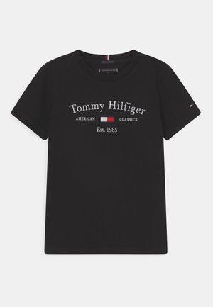 Schwarzes T-Shirt mit kurzen Ärmeln und der Aufschrift "Tommy Hilfiger American Classics Est. 1985" sowie einem rot-weiß-blauen Flaggenlogo auf Brust und Ärmel.