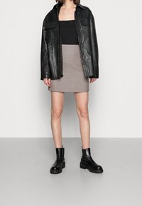 Giacca oversized in pelle nera, top aderente nero, gonna mini a fantasia con design a scacchi, e stivali neri robusti alla caviglia.