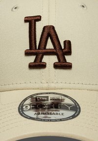 Μπεζ καπέλο με καφέ κεντημένο λογότυπο "LA". Περιλαμβάνει κυκλική ετικέτα New Era που δηλώνει "9FORTY ADJUSTABLE".