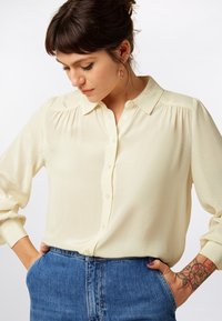 Cream-colored, lightweight blouse with a textured pattern, button-down front, and a classic collar. Long sleeves and loose fit.