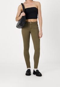 Jeans ajustados verde oliva de cintura alta, combinados con un top negro sin tirantes y un bolso negro de hombro. Textura suave, diseño ceñido.